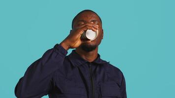 huvudskott porträtt av säkerhet ombud dricka kaffe till sluta gapande medan säkring tilldelad posta, studio bakgrund. stänga upp skott av väktare förbrukande koffeinhaltig dryck, kamera b video