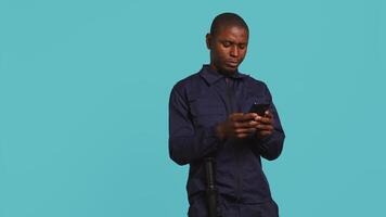 Security guard using smartphone, taking break during protection job shift. Portrait of bodyguard texting friends at work using mobile phone, isolated over studio background, camera B video