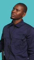 Vertical Security guard doing thinking hand gesture during surveillance shift, ensuring protection of property and personnel. Portrait of pensive man in uniform rubbing chin, studio background, camera A video