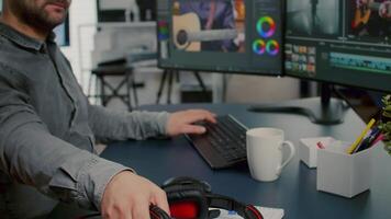 Videographer editing, cuting footage and sound on computer with dual monitors setup putting on headphones working in creative office. Man processing film montage in digital multimedia star up company. video