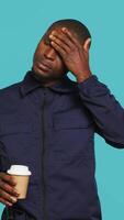 Vertical Portrait of fatigued security guard drinking coffee cup to remain energized while overseeing premises. Private law enforcement worker consuming caffeinated beverage, studio backdrop, camera A video