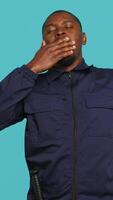 Vertical Tired security guard yawning while being tasked with preventing criminal activity and detaining suspects. Portrait of bodyguard showing exhaustion signs during night shift, studio background, camera A video
