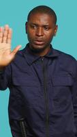 Vertical Security guard doing stop sign gesturing, being tasked with preventing criminal activity and detaining suspects. Portrait of stern bodyguard showing halt hand gesture, studio background, camera A video