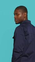 Vertical Security guard turning around after hearing suspect sounds during surveillance shift, ensuring protection. Portrait of man in uniform standing isolated with back against studio background, camera A video