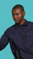 Vertical Portrait of security agent pointing finger at people, warning them while securing assigned post, studio background. African american guardian scolding trespassers, handling security breaches, camera A video