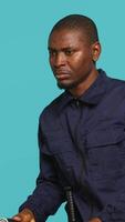 Vertical Portrait of security agent securing assigned post, turning on flashlight, studio background. African american guardian prepared to handle security breaches, using lantern device, camera A video