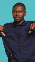 Vertical Portrait of security guard doing thumbs down sign gesturing, denying access while overseeing premises. Private law enforcement worker doing negative hand gesture, studio backdrop, camera A video