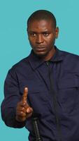 Vertical Portrait of security guard doing no gesturing with finger, prohibiting access while overseeing premises. Private law enforcement worker barring people from entering place, studio backdrop, camera A video