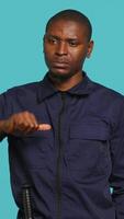 Vertical Portrait of security agent doing thumbs down sign gesturing, refusing entry while securing assigned post, studio background. Guardian doing negative hand gesture, handling security breaches, camera A video