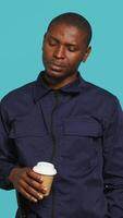 Vertical Portrait of security agent uses coffee cup to remain energized while securing assigned post, studio background. Guardian consuming caffeinated beverage to be able to handle security breaches, camera A video