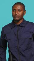 Vertical Portrait of security guard overseeing premises to prevent intrusion pretending to shoot gun. Private law enforcement worker doing pistol fingers hand gesture, studio backdrop, camera A video