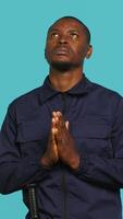 Vertical Portrait of security guard waiting for miracle, putting hands together while overseeing premises. Private law enforcement worker looking to sky, praying, studio backdrop, camera A video