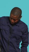Vertical Portrait of security agent removing baton from belt, using it to secure assigned post, studio background. African american guardian pointing finger to truncheon, handling security breaches, camera A video