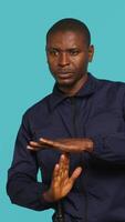 Vertical Security guard doing time out sign gesturing, being tasked with ceasing unwanted access. Portrait of stern bodyguard showing pause hand gesture, doing interrupting gesture, studio background, camera A video