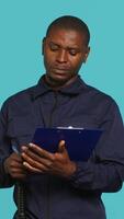 Vertical Portrait of security guard holding clipboard, taking notes while overseeing premises. Private law enforcement worker using pen to write down orders received, studio backdrop, camera A video