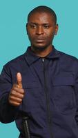 Vertical Happy security guard doing thumbs up sign gesturing with finger, preventing public access in restricted area. Portrait of smiling bodyguard doing positive hand gesture, studio background, camera A video