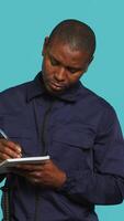 Vertical Portrait of security guard using notepad to take notes of suspicious activity while overseeing premises. Private law enforcement worker documenting security protocols, studio backdrop, camera A video