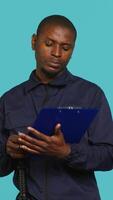 Vertical Security guard holding clipboard, taking notes, receiving orders during protection job shift. Portrait of bodyguard using pen to write informations received, studio background, camera A video