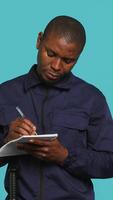 Vertical Security guard with notepad taking notes, receiving orders about suspects to look out. Portrait of bodyguard using pen, documenting layout location in need of protection, studio background, camera A video