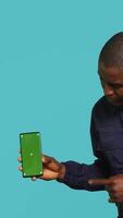 Vertical Portrait of security agent presenting mockup phone and securing assigned post, studio background. Guardian showing green screen smartphone while handling security breaches video
