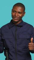 Vertical Portrait of joyous security guard doing thumbs up sign gesturing with finger while overseeing premises. Private law enforcement worker doing positive hand gesture, studio backdrop, camera A video