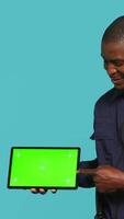 Vertical Portrait of happy security staff member showing isolated screen tablet. Joyous patrolling agent maintains secure environment, showcasing chroma key device, studio background, camera A video