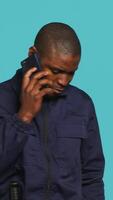 Vertical Portrait of security guard at work using phone to make call to friends while overseeing premises. Private law enforcement worker in telephone call with mates, studio backdrop, camera A video