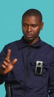 Vertical Security guard preventing criminal activity, threatening suspects with active bodycam. Portrait of menacing bodyguard pointing towards security body camera, studio background, camera A video
