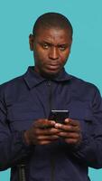 Vertical Security guard using smartphone, taking break during protection job shift. Portrait of bodyguard texting friends at work using mobile phone, isolated over studio background, camera A video