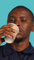 Vertical Headshot portrait of security agent drinking coffee to stop yawning while securing assigned post, studio background. Close up shot of guardian consuming caffeinated beverage, camera A video