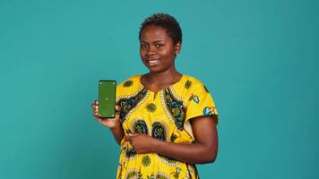 Young confident woman presenting a green screen on smartphone, working in studio on an advertisement. Smiling natural girl holds a phone with isolated chroma key display. Camera A. video