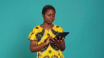 Happy positive adult navigating on online webpages in studio, using portable gadget to browse things on internet connection. Woman in traditional ethnic attire poses against background. Camera A. video