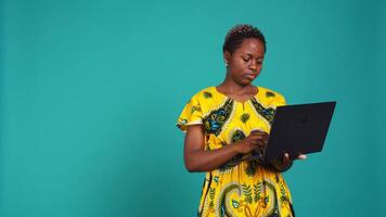 Young woman freelancer navigating on online webpages in studio, browsing information on device connected to internet. Charming traditional girl carries a portable pc. Camera B. video