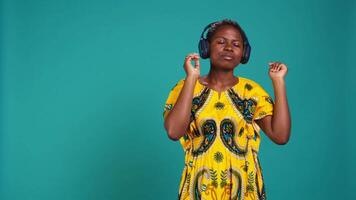 Carefree relaxed woman listening to music and dancing in the studio, having fun with a new groovy playlist. Happy optimistic person enjoys radio songs on her audio headset. Camera B. video