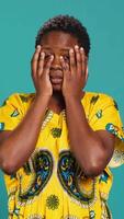 Vertical Horrified young woman covering her eyes to avoid seeing something, feeling squeamish and appalled about a thing in studio. Being disgusted and shocked in ethnic clothing. Camera A. video