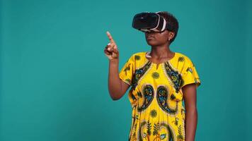 Gorgeous girl in ethnic clothes using vr glasses against blue background, working with high tech 3d experience with virtual reality device. Young woman using smart headset. Camera B. video