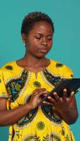 Vertical Happy positive adult navigating on online webpages in studio, using portable gadget to browse things on internet connection. Woman in traditional ethnic attire poses against background. Camera A. video