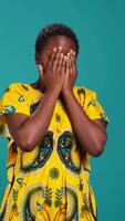 Vertical Horrified young woman covering her eyes to avoid seeing something, feeling squeamish and appalled about a thing in studio. Being disgusted and shocked in ethnic clothing. Camera B. video