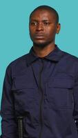 Vertical Security guard does surveillance for various organizations and venues, ensuring protection of property and personnel, studio background. Portrait of intimidating man in uniform crossing arms, camera A video