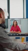 Videographer in web online conference with project manager on call editing client work, getting feedback on commercial movie using post production software on two monitors in start up office video