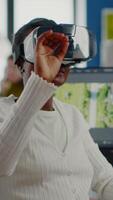 Black videographer wearing VR headset editing project in production studio office. maker employee processing film montage in digital multimedia company while, colleagues working in background video