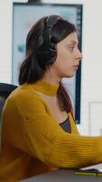 Photo editor with headphones retouching image using stylus pen, drinking coffee, working on PC with two displays. Woman retoucher editing in software app with graphic tablet sitting in creative agency video