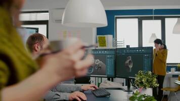 Mechanical engineer working on computer designing in CAD software 3D model of engine while african coworker asking help. Man using pc with two monitors innovating motor prototype in creative agency video
