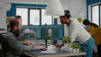 multiétnico equipe discutindo sobre industrial projeto usando dual monitores configuração para desing 3d metálico peças dentro cafajeste Programas. industrial engenheiro e africano Gerente trabalhando juntos dentro criativo escritório video