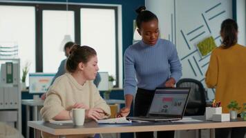 African american startup employee standing next to coworker presenting marketing strategy on laptop with charts and statistics. Colleagues working on group project analyzing business market share. video
