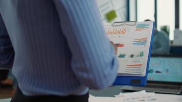 Closeup of african american woman hands holding clipboard with financial data and sales charts in startup office. Focused employee analyzing performance indicators reading business statistics. video