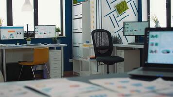 Empty startup office with multiple computer screens displaying financial statistics and closeup on laptop with moving charts on desk. Selective focus on portable computer with business erp software. video