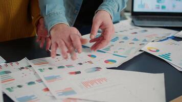 Selective focus on colleagues comparing marketing statistics and working on business strategy at desk with laptop. Detail view of coworkers hands going through papers with sales charts. video