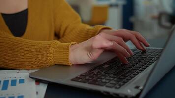 Closeup on woman hands typing on laptop keyboard and smiling at camera sitting at desk in startup office. Portrait of casual employee working relaxed with portable computer in business workplace. video
