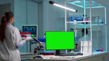 Team of scientists working in background of modern laboratory using computer with green screen, mockup display, chroma key monitor, analysing experiment evolution, high tech development lab. video